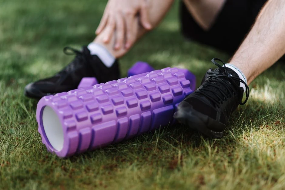 Athlete seated on grass beside black running shoes and a purple foam roller.